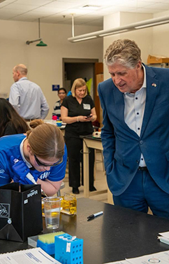 older man watching female student work on a biotech project in a high school classroom