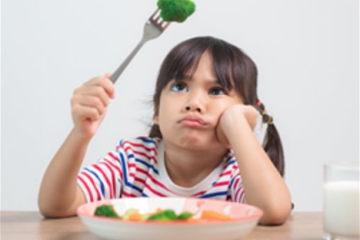 Young unhappy girl holding a piece of broccoli over her head