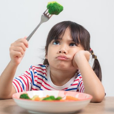 Young unhappy girl holding a piece of broccoli over her head